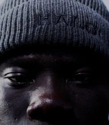 Close-up portrait of a Black man wearing a grey ribbed knit beanie photographed by Dennis Stenild.