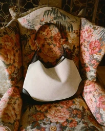 A cream and dark brown leather handbag resting on an ornate floral upholstered armchair in New York by Dennis Stenild.