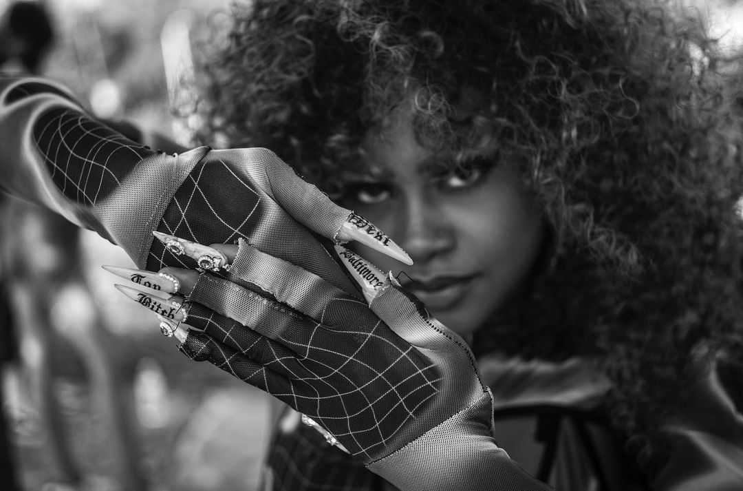 Striking black and white portrait of a Black woman with afro, showcasing creative mesh gloves and statement fingernails, close-up.