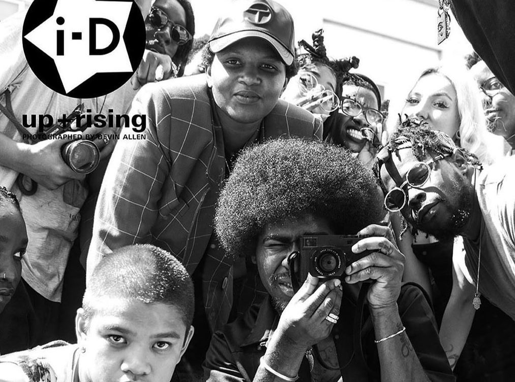 Monochrome image capturing a diverse group of people, including a photographer with a camera, in an outdoor setting with magazine branding.