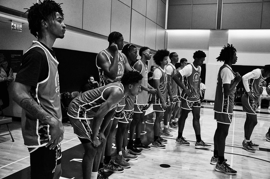 A line of basketball players in jerseys stand on a court in a black and white photo, with the first player facing forward.