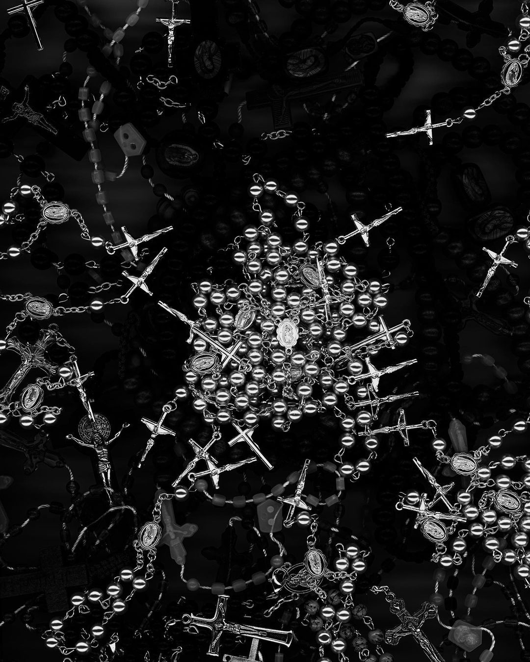Monochrome image featuring a dense scattering of rosary beads, each with a crucifix, creating an intricate pattern on a black background.