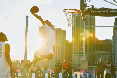 Basketball player mid-air dunking a basketball against a city skyline at sunset, photographed by Devin Allen.