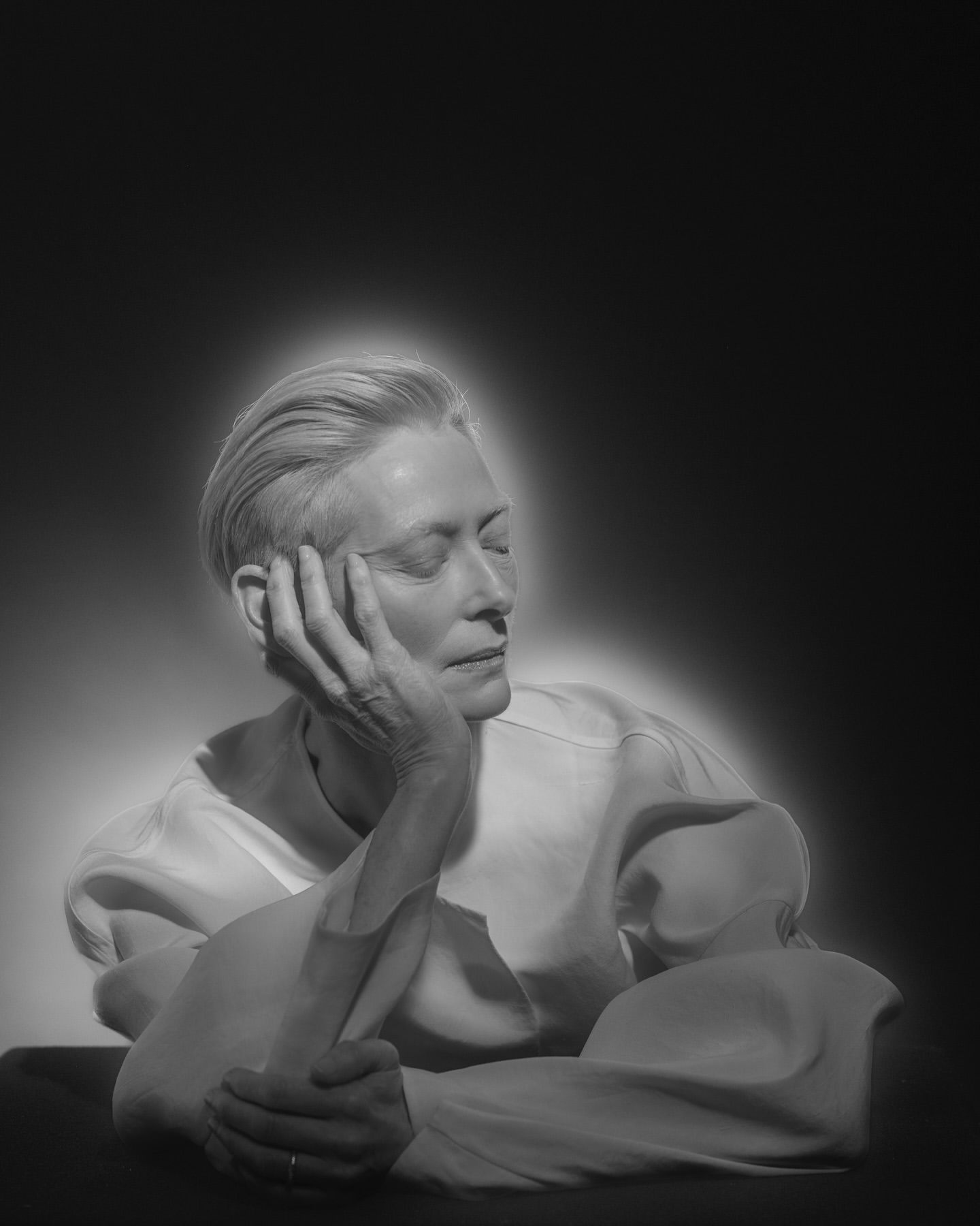 Monochrome portrait of an adult woman with short blond hair, gazing to the right with her face resting on her left hand.