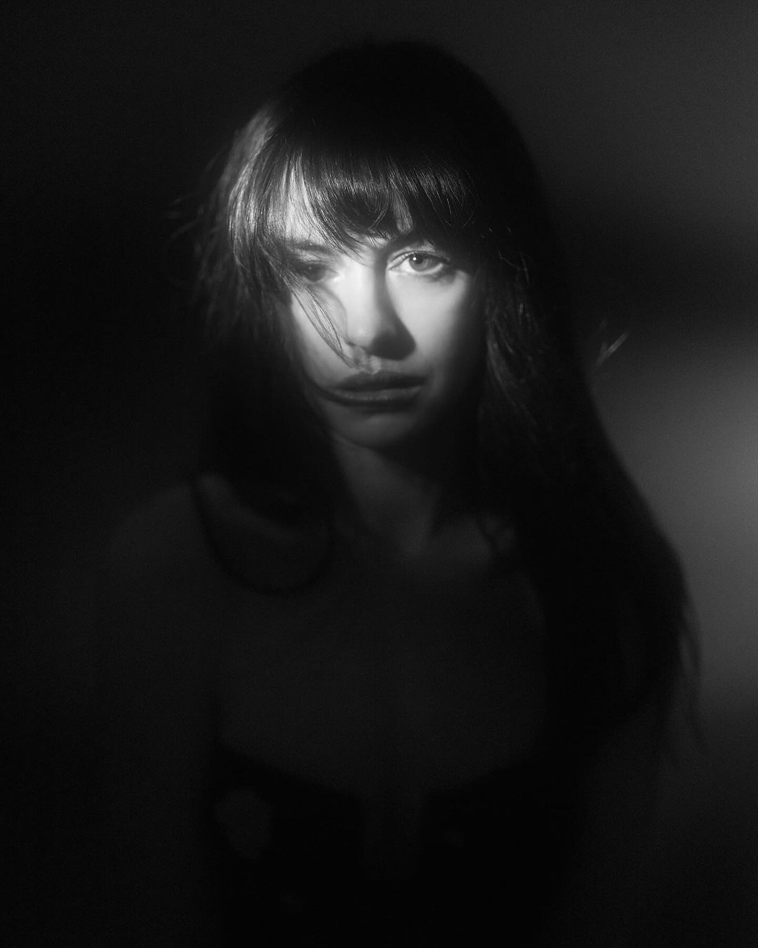 Portrait of a woman with long dark hair and bangs in dramatic low-key lighting by photographer Devin Yalkin.