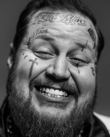 Close-up black and white portrait of a smiling man with facial tattoos and grillz, photographed by Devin Yalkin.