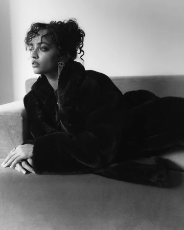 Monochrome portrait of a woman with curly hair wearing a dark faux fur coat while reclining on a sofa
