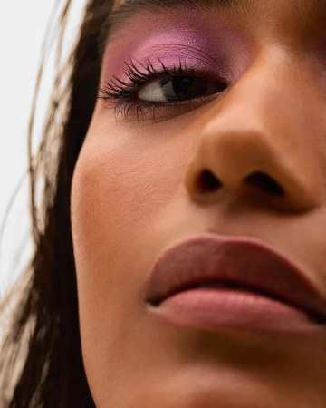 Close-up beauty shot featuring an adult female with pink eyeshadow and lipstick against a white background, emphasizing makeup details.