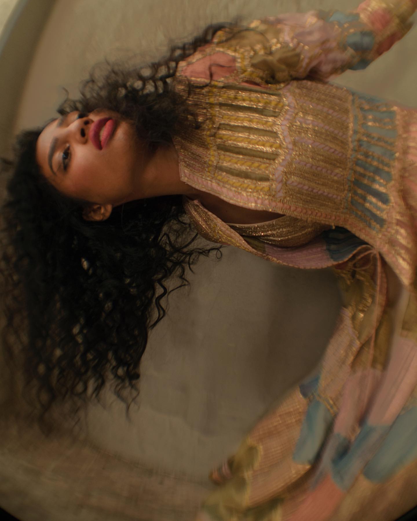 Woman with long dark curly hair wearing an ornate patterned dress captured in a low-angle vertical portrait