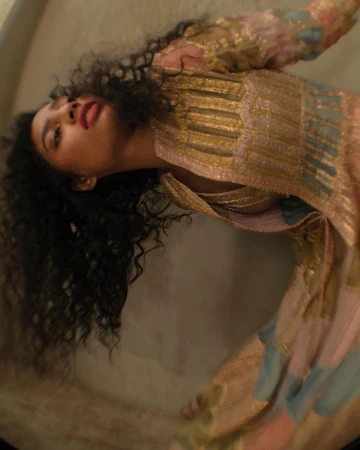 Woman with long dark curly hair wearing an ornate patterned dress captured in a low-angle vertical portrait