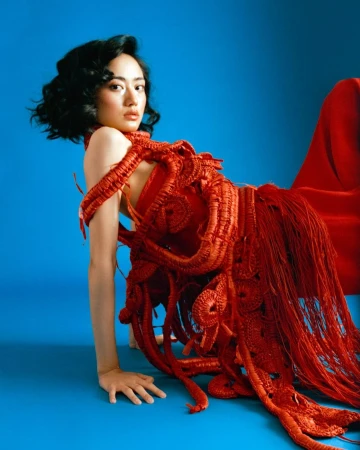 Woman in textured red crocheted dress posing against a vibrant blue studio backdrop by photographer Dhruvin