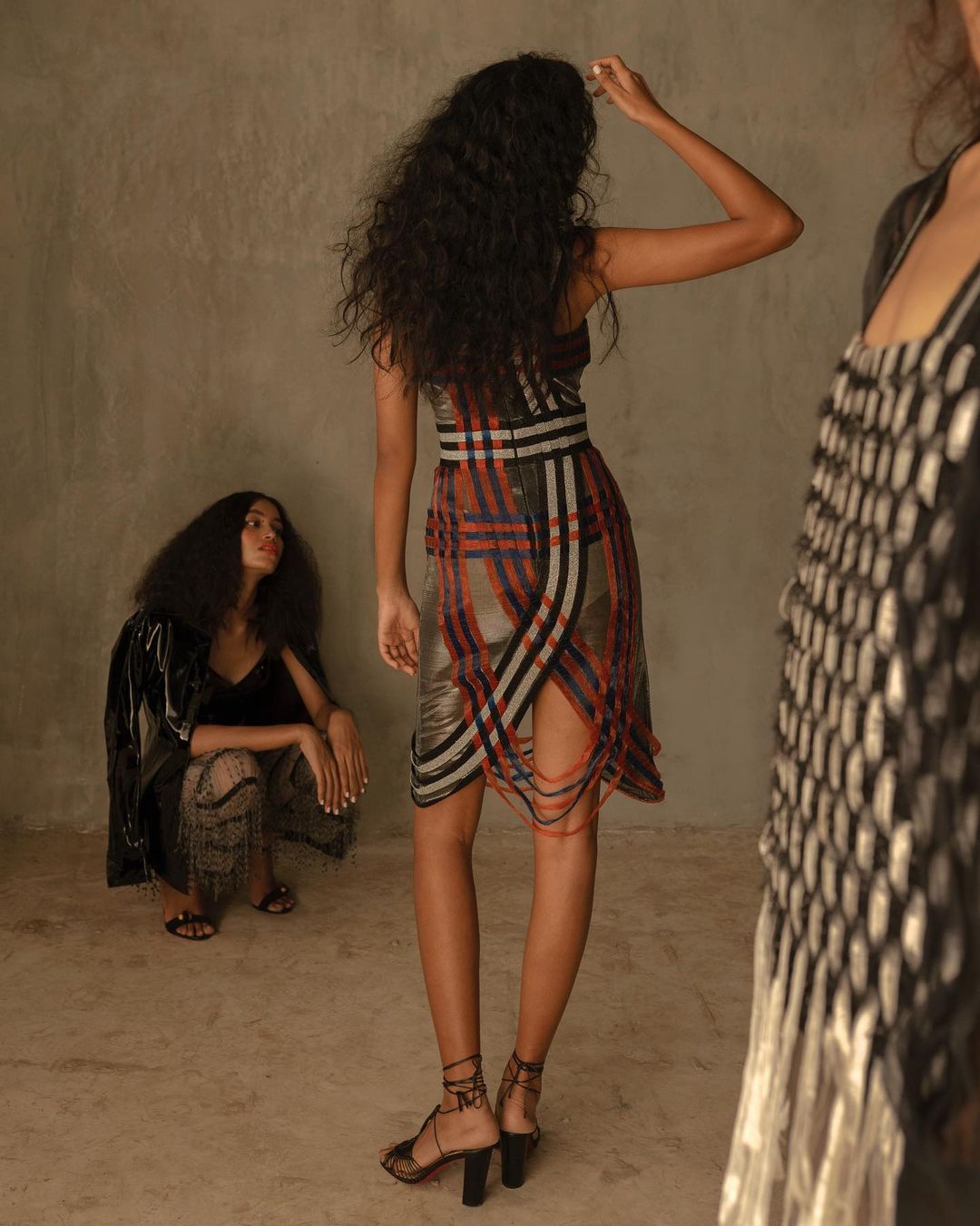 Three women in a photo studio. One is crouched while the others are standing. One is wearing a fashionable plaid dress and heels.