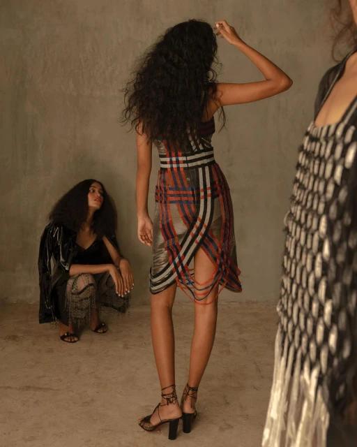 Three women in a photo studio. One is crouched while the others are standing. One is wearing a fashionable plaid dress and heels.