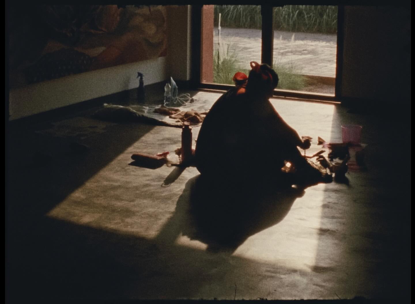 Silhouette of a person seated on the floor in a room with sunlight streaming through the windows, next to cleaning supplies.