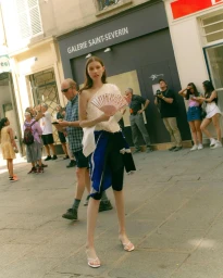 A young female model holding a pink folding fan on a sunny street, photographed by Dhruvin