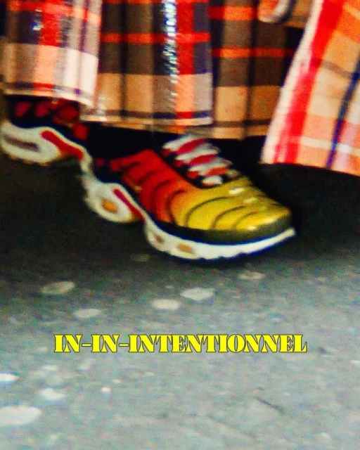 Close-up of multicolor sneakers with orange, yellow, and white on a grey surface with a plaid textile in the background.