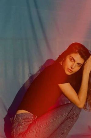 Woman in dark t-shirt and blue jeans squatting against a textured fabric backdrop
