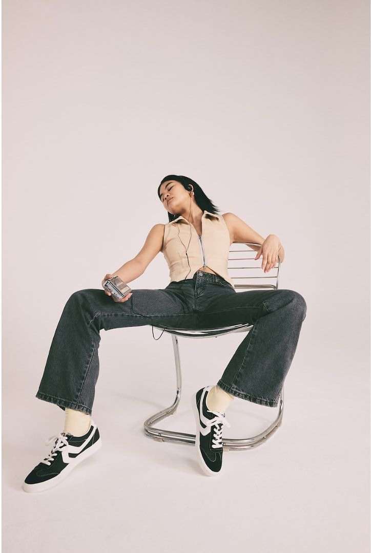 Woman in casual outfit seated on chair holding retro cassette player in studio with white backdrop in fashion photography