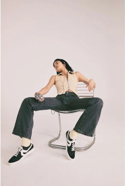 Woman in casual outfit seated on chair holding retro cassette player in studio with white backdrop in fashion photography