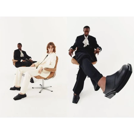 Two models seated in wheeled office chairs against a plain white background, photographed by Diane Sagnier in Paris.