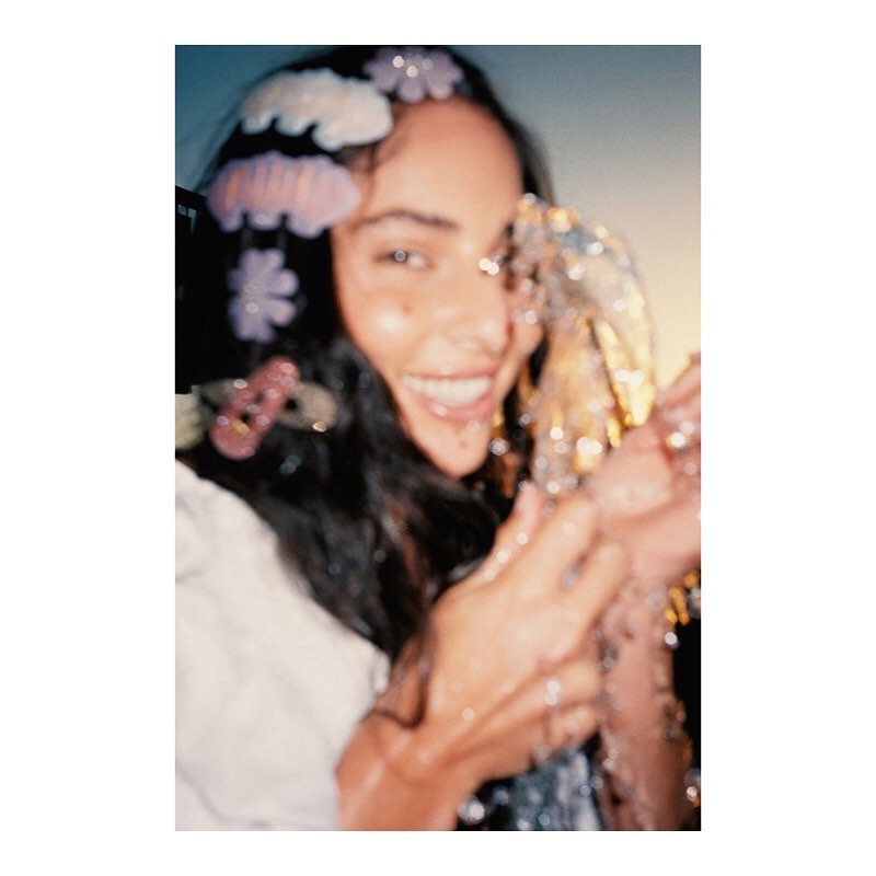 Portrait of a woman with dark hair and multiple flower-shaped hair accessories, smiling with confetti, shot with shallow depth of field.