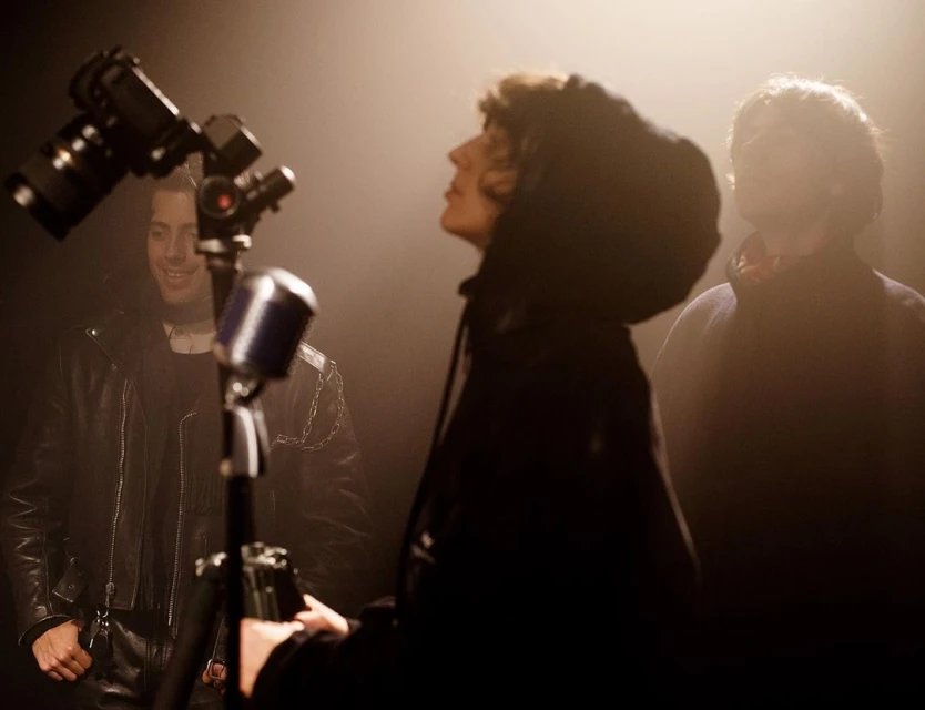 Three men in a music studio setting with vintage microphone, camera, and soft lighting, creating a moody and vintage atmosphere.
