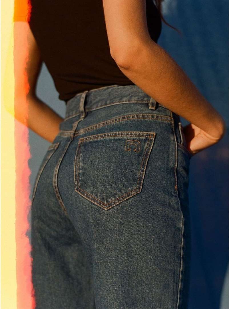 Close-up studio shot of an adult female wearing blue jeans and a black tank top, with sunlight and color gels creating a vibrant background.