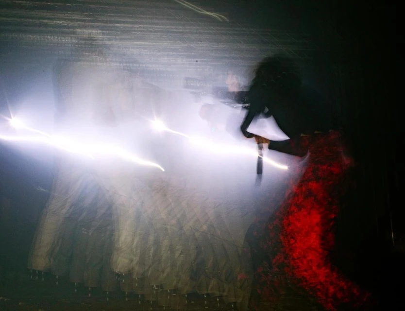 Blurred image of a person in a red dress dancing in a dark environment with streaks of light painting a dramatic and energetic scene.