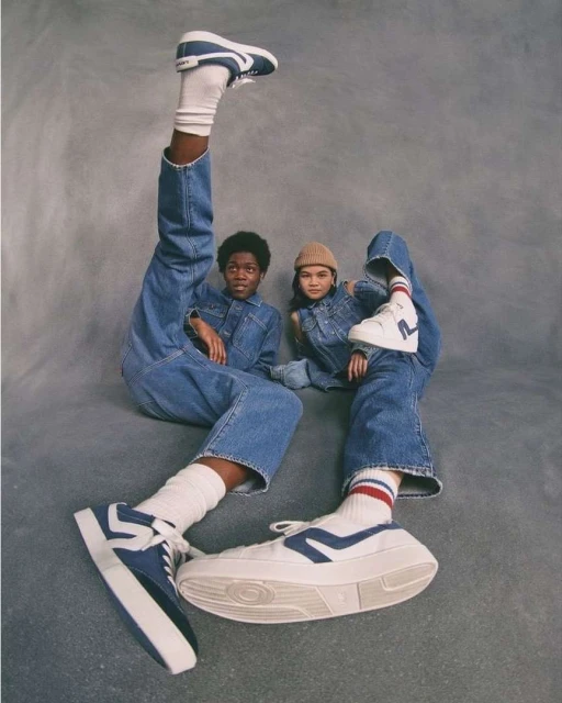 Two children model apparel and white platform sneakers in a studio shot, one with leg raised, against gray backdrop.