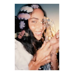 Portrait of a smiling young woman wearing decorative hair clips and holding a crystal object, photographed by Diane Sagnier.