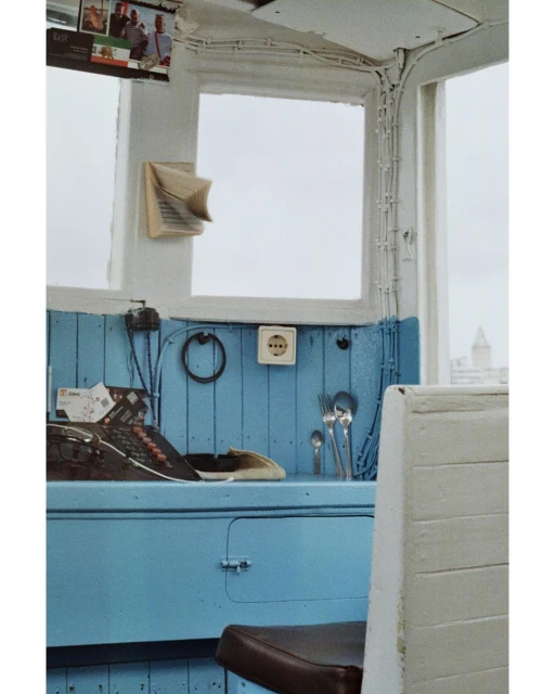 Interior view featuring a retro cash register, utensils, and a blue counter near a window, capturing a nostalgic scene indoors.