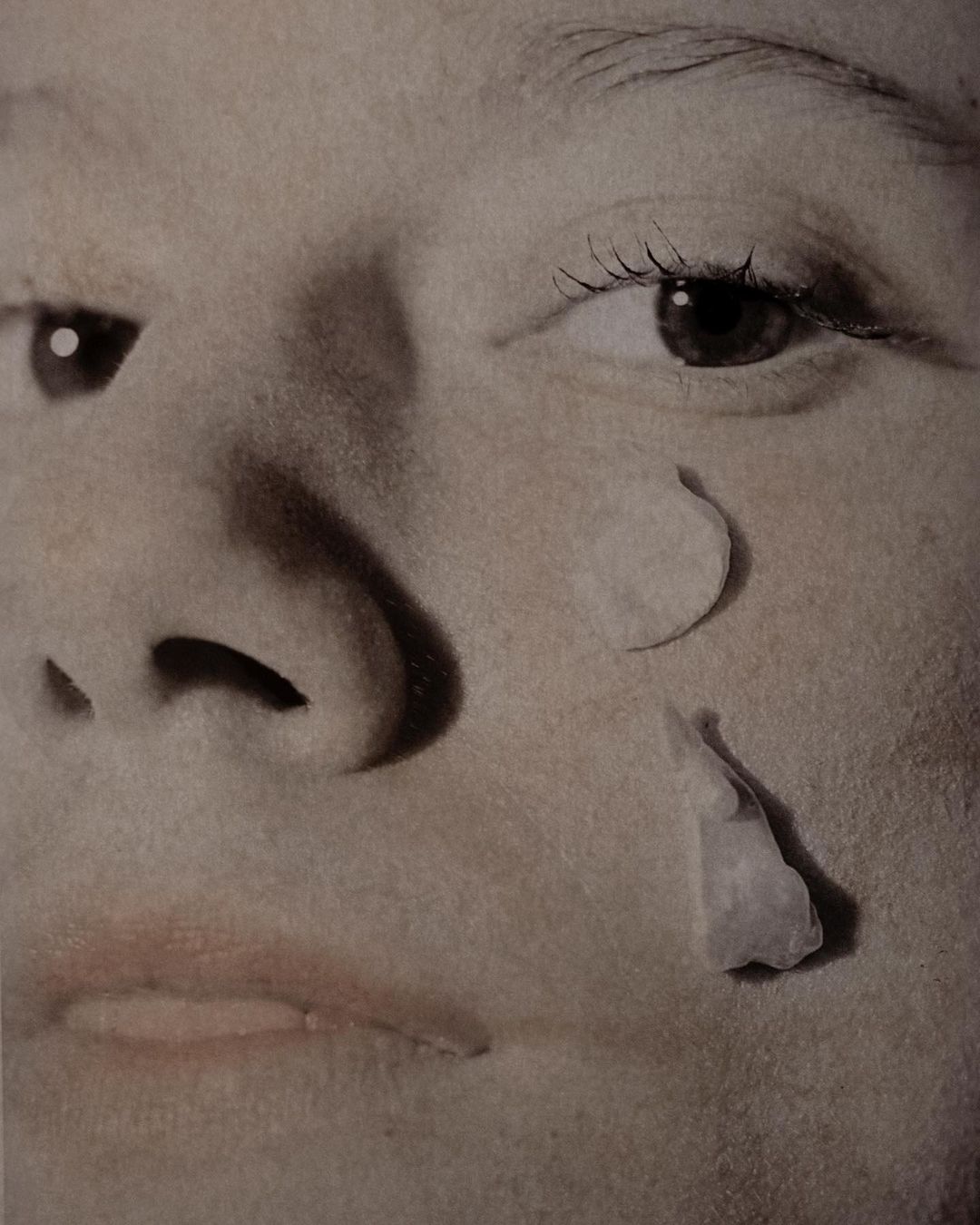 Close-up of a young adult's face, featuring dramatic tears crafted from cut paper, emphasizing the texture and artistic presentation.