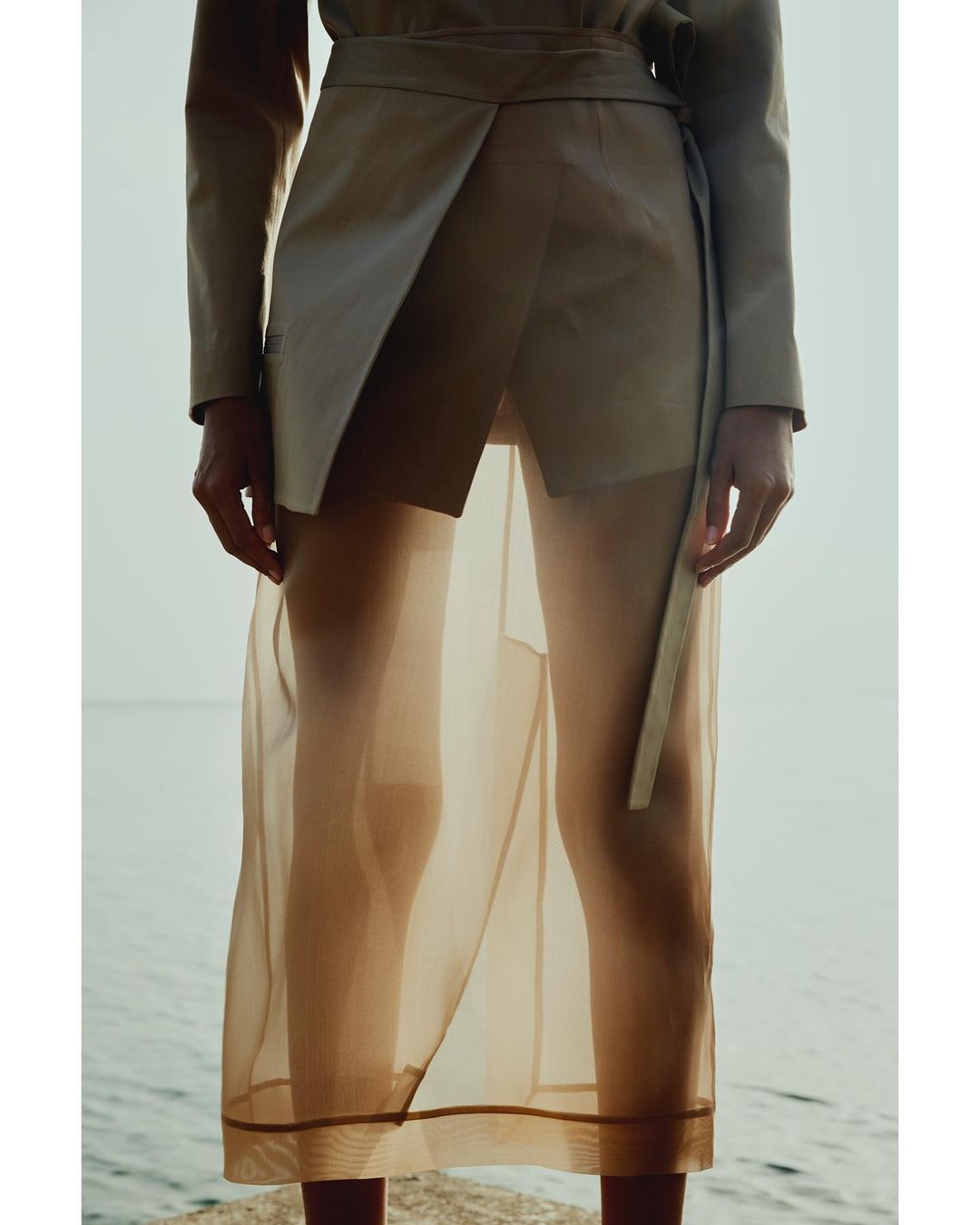 Close-up of a person wearing a beige tailored jacket with a sheer skirt standing by water in Paris.