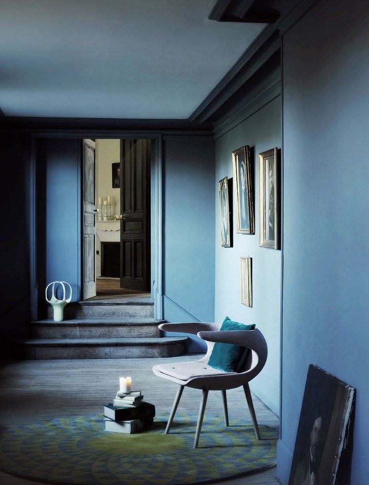 Interior design: chair, books, candles, and framed art in a room with blue walls, doorway, and stairs; soft, diffused lighting.