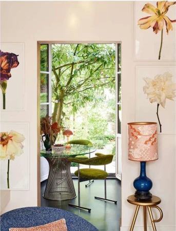 Living room corner with a modern glass table, green chairs, flower pictures, and a lamp on a table, creating a stylish home interior.