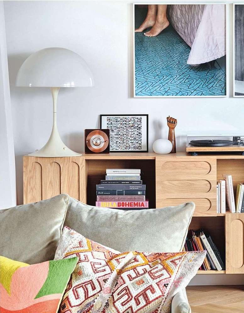 Interior view of living room with throw pillows on a sofa, a modern lamp on a wooden cabinet displaying art, books, and a record player.