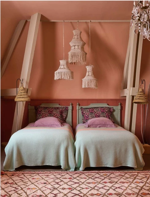 Bedroom with two twin beds, floral pillows, and macrame pendant lights in a cozy indoor setting, creating a warm and inviting atmosphere.