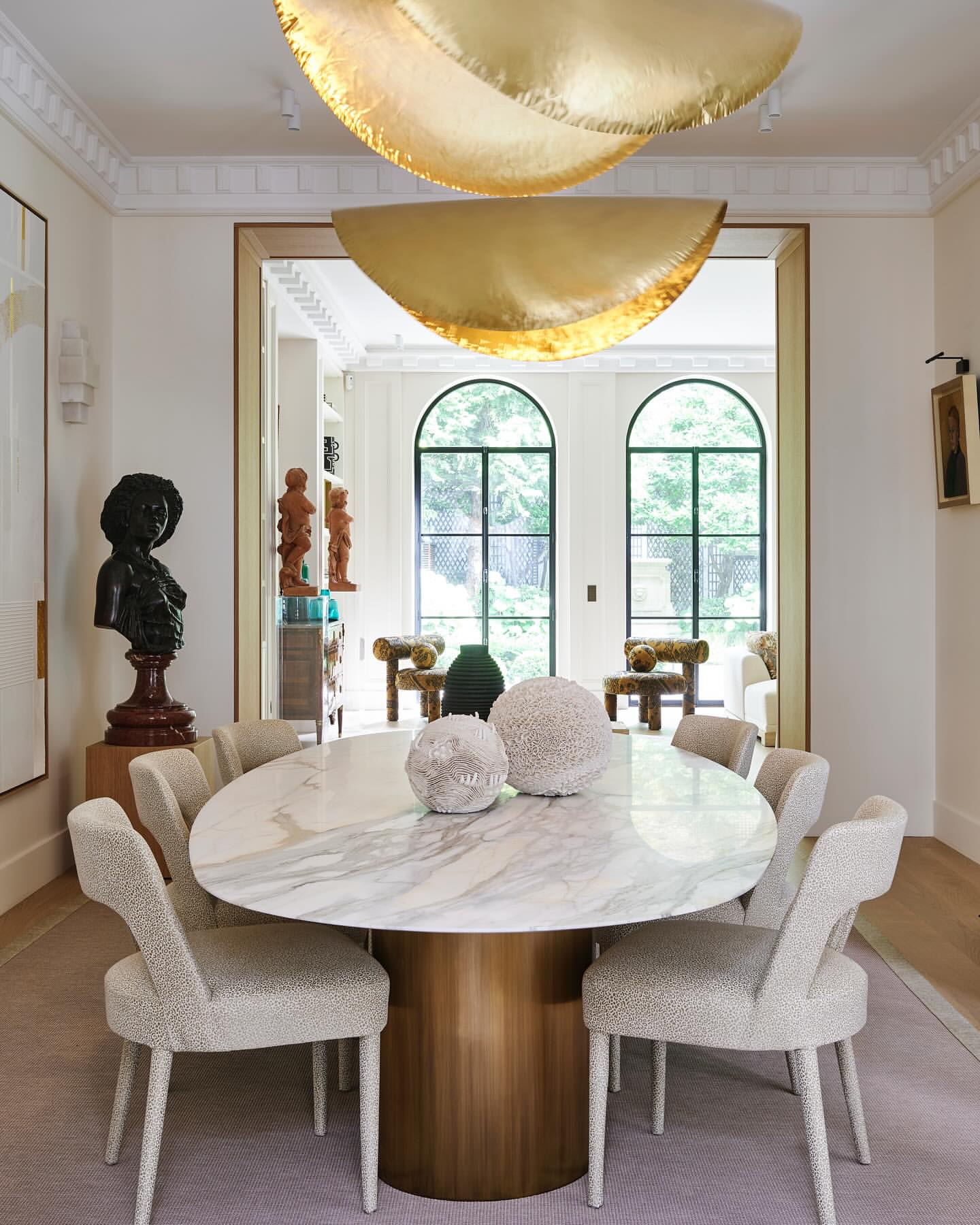 Dining room interior with marble table, upholstered chairs, and a gold sculptural chandelier, creating a luxurious and modern space.