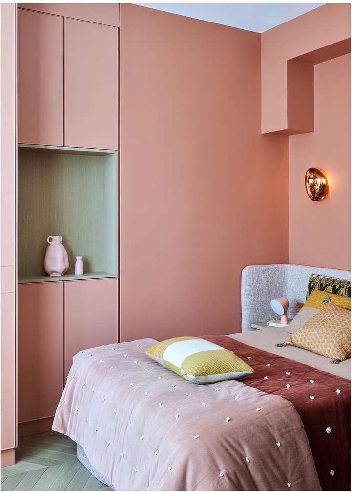 Modern bedroom interior with a pink color palette featuring a bed with pillows, a wall, and cabinets with decor items.