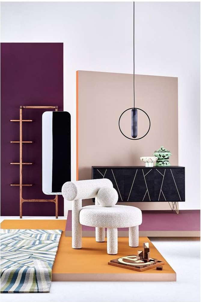 Interior design shoot of a white boucle chair, dark wood cabinet, and minimalist decor against colorful geometric background panels.