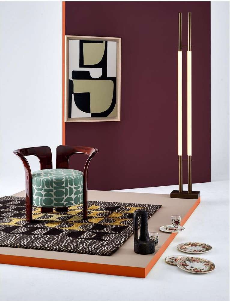 Modern interior setup featuring a wood-frame chair with geometric-print cushion, abstract wall art, sleek floor lamp, and vintage dishware.