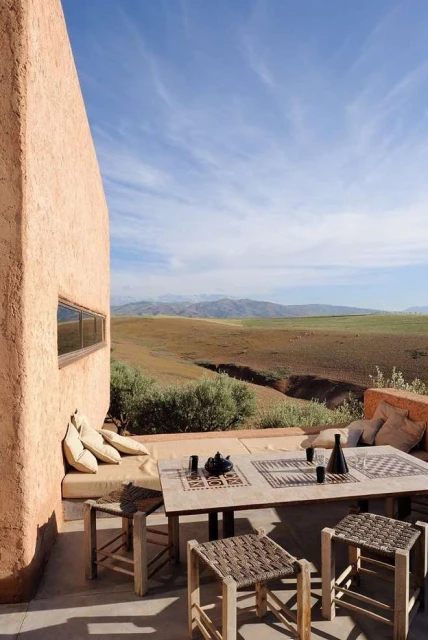 Outdoor patio with table and chairs overlooks a scenic landscape featuring rolling hills and a partly cloudy blue sky.