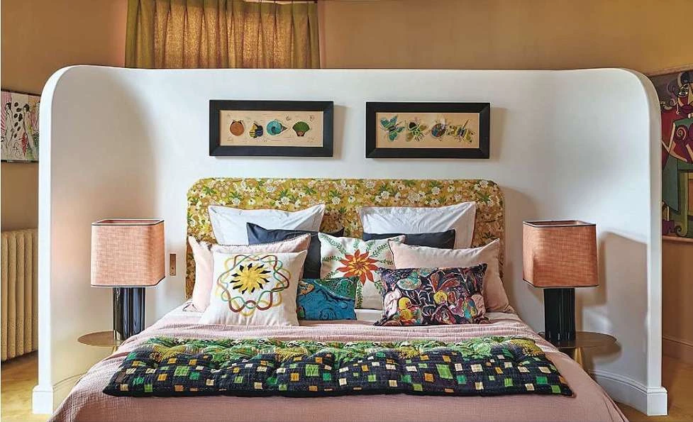 Bedroom interior with a double bed featuring colorful pillows and a patterned headboard, complemented by framed art and two table lamps.