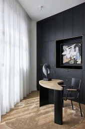 Modern home office with black built-in cabinetry, a curved wooden desk, and a sculptural art piece by photographer Didier Delmas
