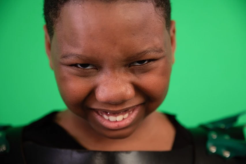 Close-up shot of a smiling Black child in dark clothing against a vibrant green background, highlighting skin tone and texture.
