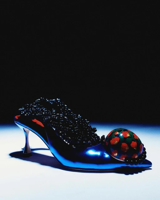 Elegant shoe with intricate beaded embellishments and a painted ball accent, displayed against a dark background, creating a striking contrast.
