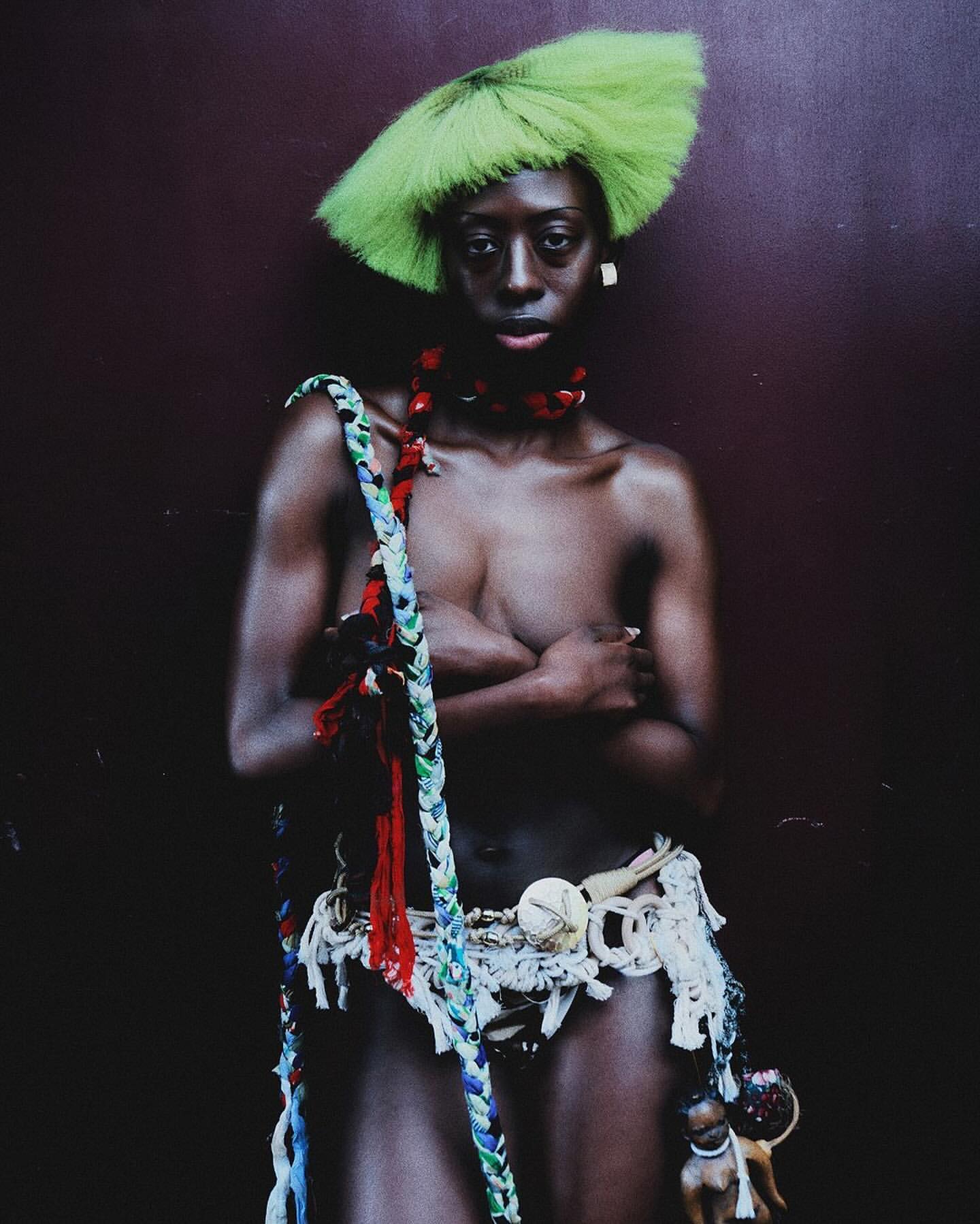 Striking portrait of a woman with green hair and tribal-inspired accessories against a dark textured wall, expressive and culturally rich.