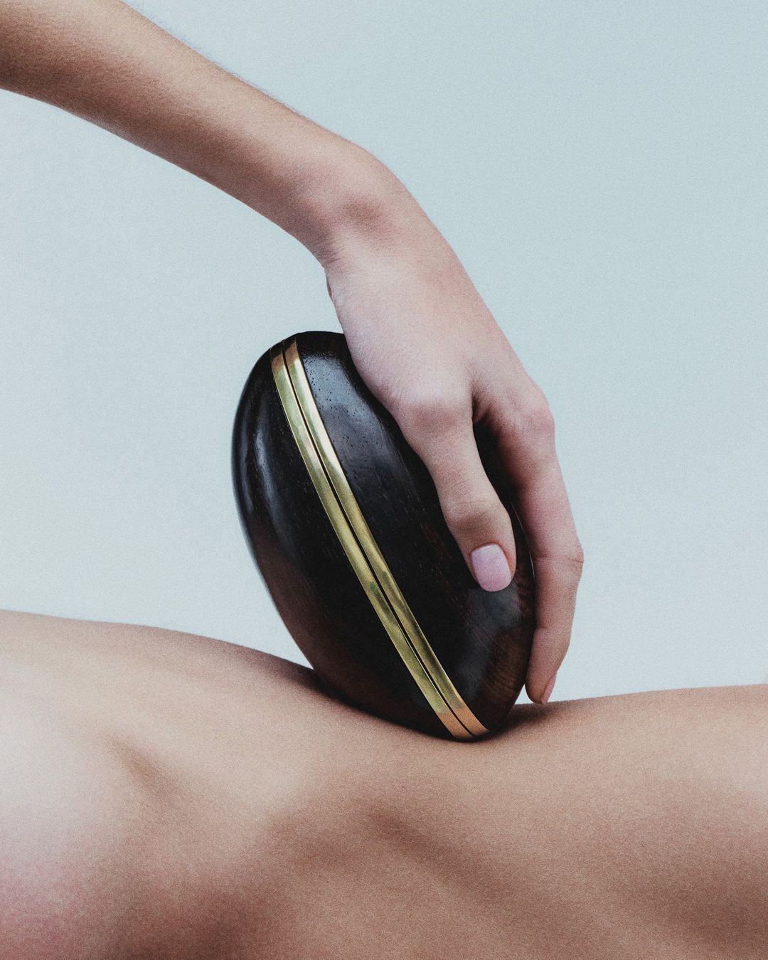 Wooden Gua Sha massage tool being used on a person's back, promoting wellness and relaxation in a minimalist studio setting.