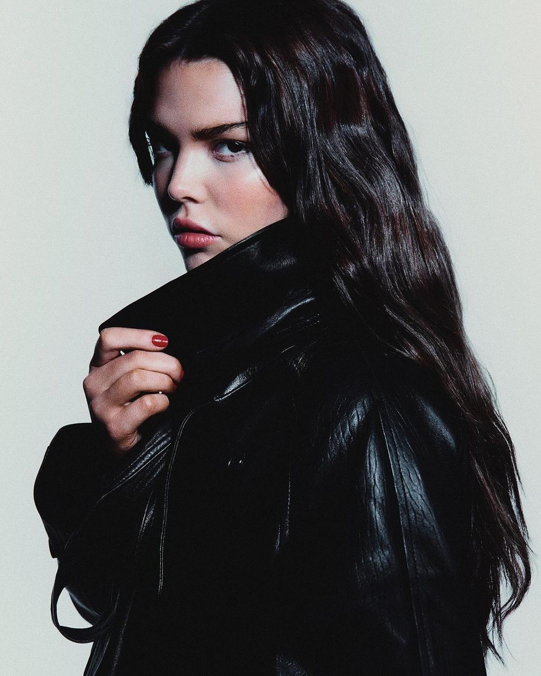 Portrait of a woman with long dark hair wearing a black leather jacket against a light background