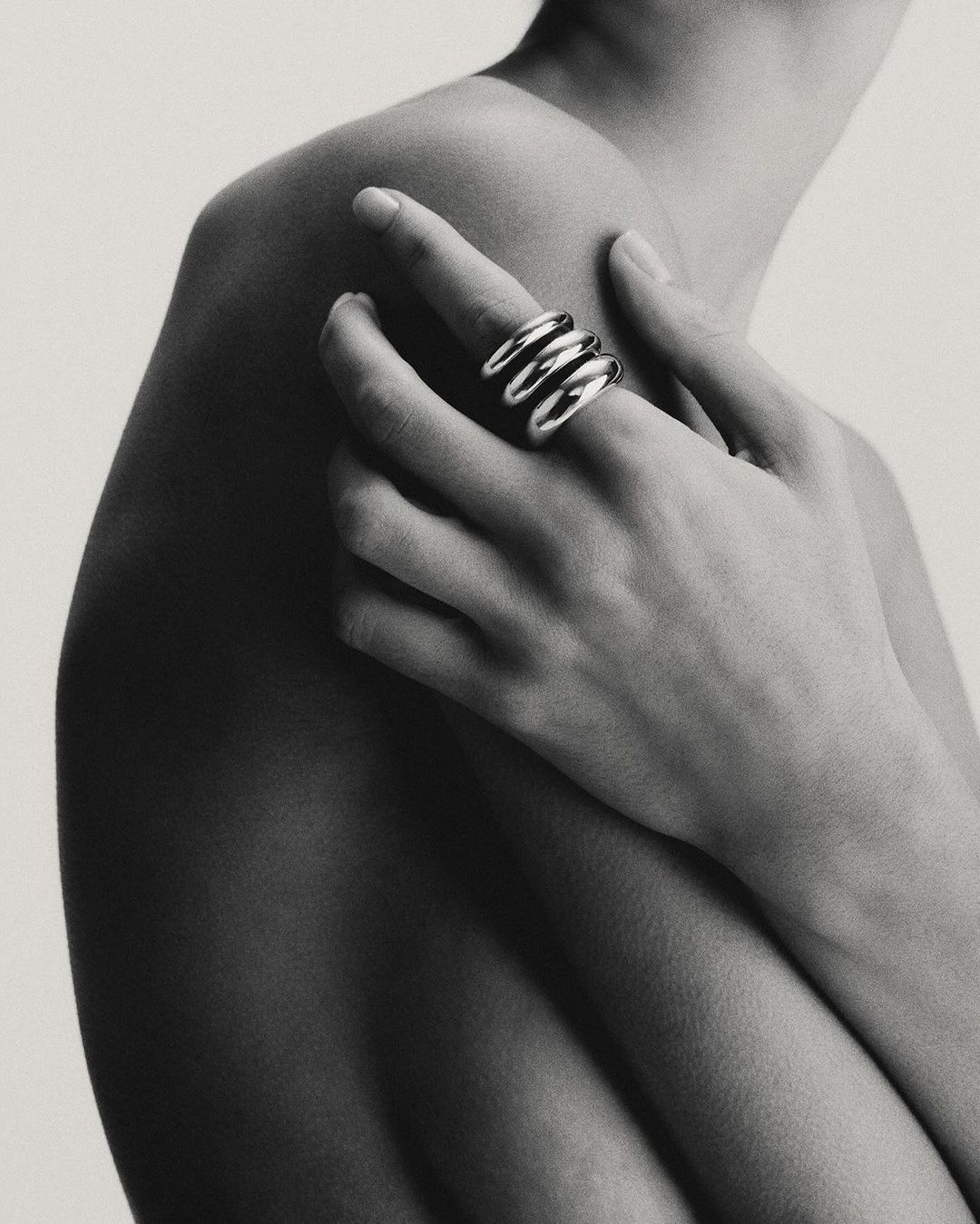 Close-up portrait of a person wearing three stacked silver rings on a finger resting against their bare shoulder.